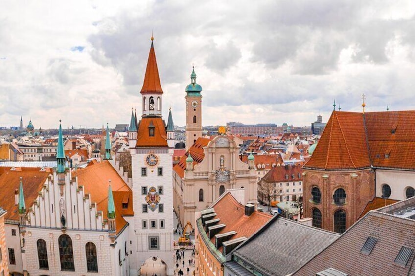 A cityscape with historic buildings, a prominent clock tower, and a church with a spire. 2