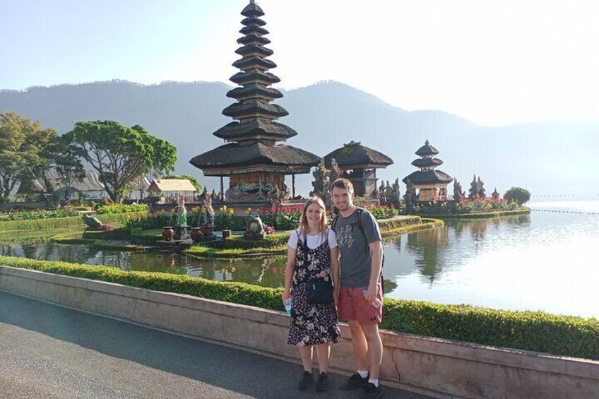 A couple standing by a pond with pagodas and mountains in the background. 1