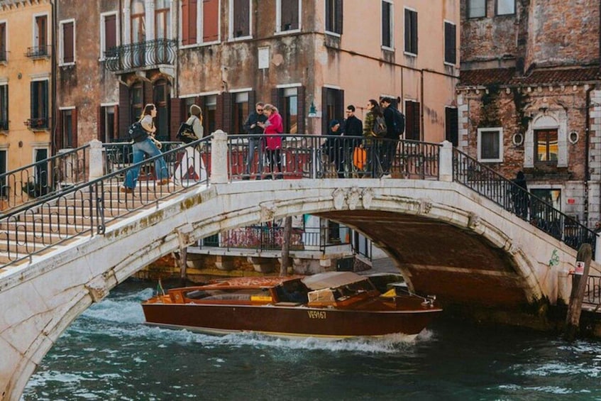 A boat on a canal under a bridge with people on the bridge. 3