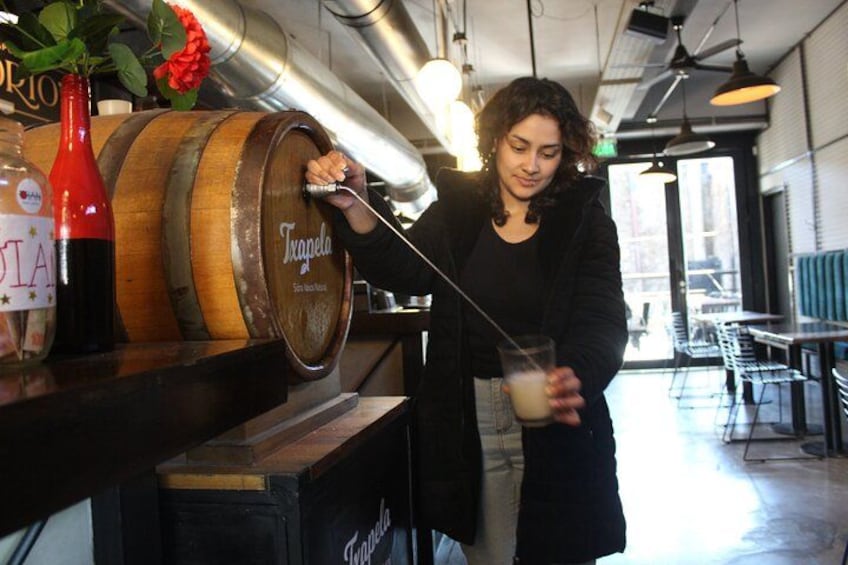 A person pouring a drink from a wooden barrel labeled 'Trapezoid' into a glass. 4