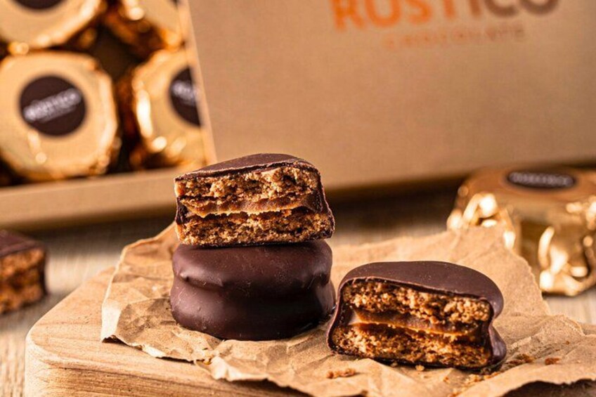 A stack of chocolate-covered treats on parchment paper, with a box labeled 'ROSTICO' in the background. 2