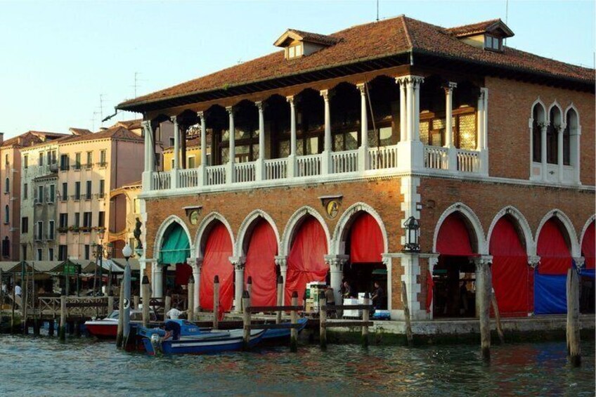 A historic building with arched windows and a balcony, situated by a canal with boats. 3