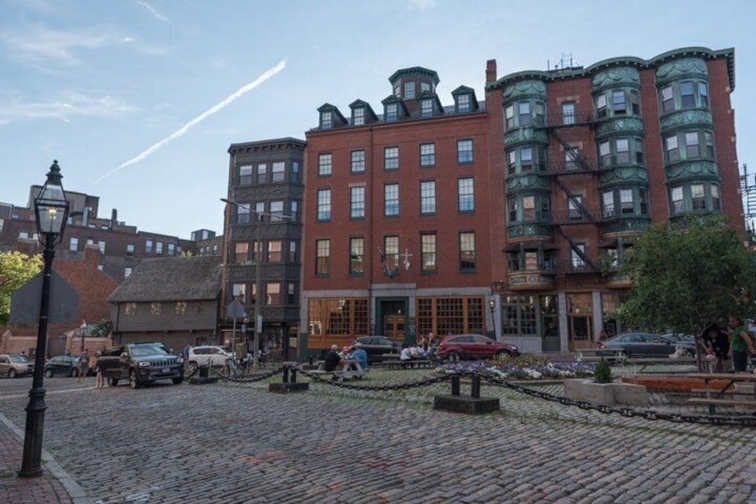 A cobblestone street with historic buildings, a street lamp, and parked cars. 4