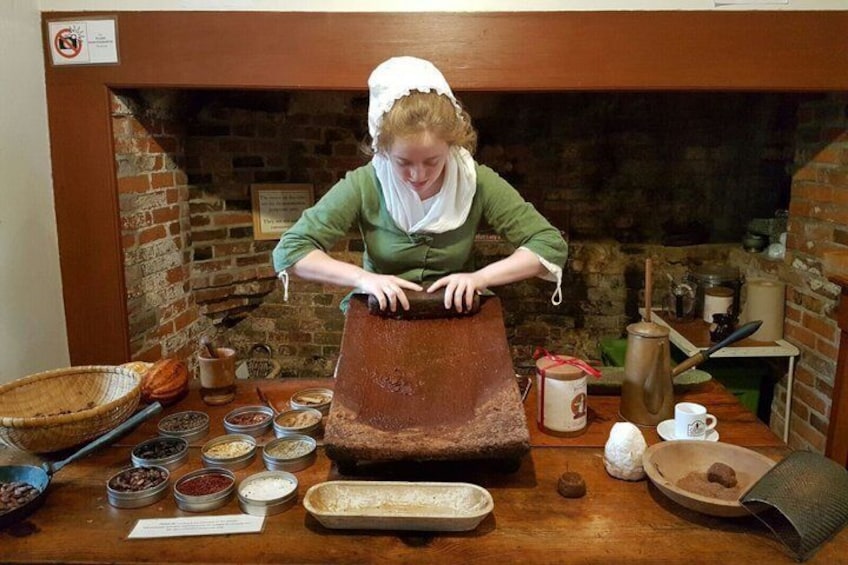 A person using a traditional wooden millstone, surrounded by historical cooking utensils and containers. 5