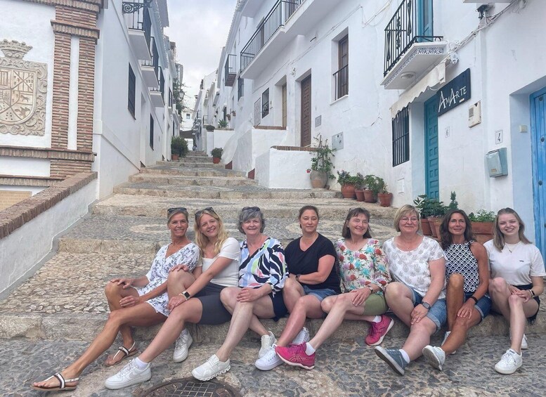 A group of people sitting on stone steps in a narrow street with white buildings and blue doors. 2