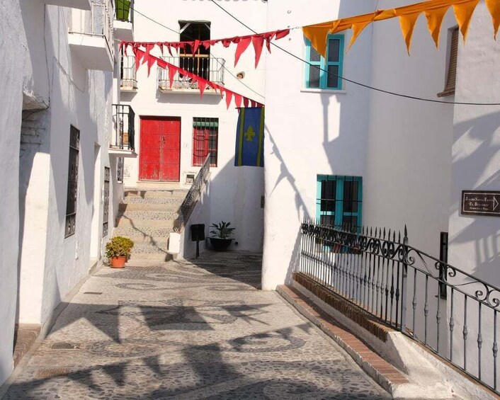 A narrow street with white buildings, red doors, and blue windows. 4