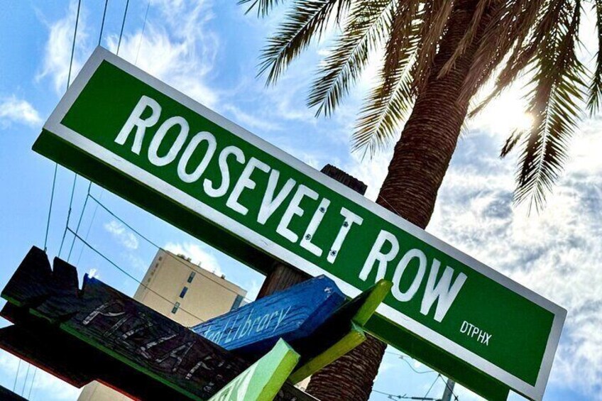 A street sign for Roosevelt Row with a palm tree and a building in the background. 3