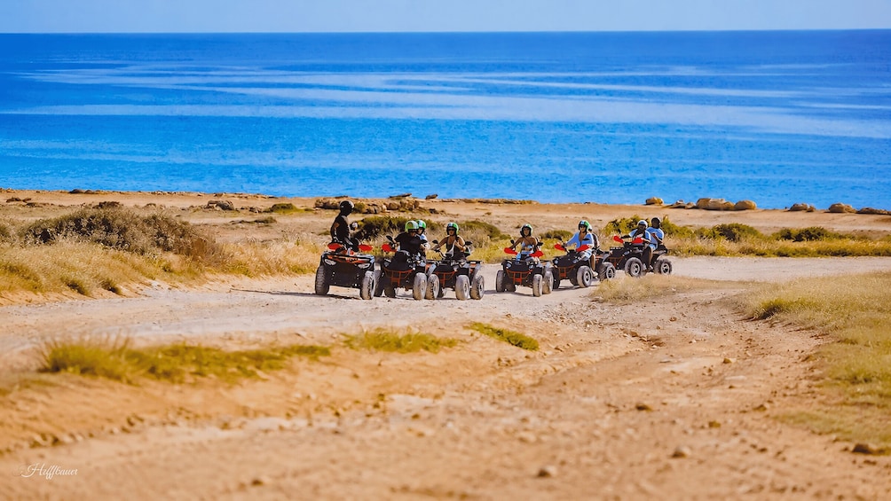 A group of people on quad bikes on a dirt path near the ocean. 2