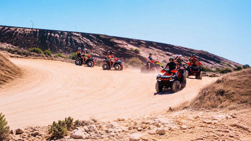A group of people riding ATVs on a dirt road in a hilly, arid landscape. 1