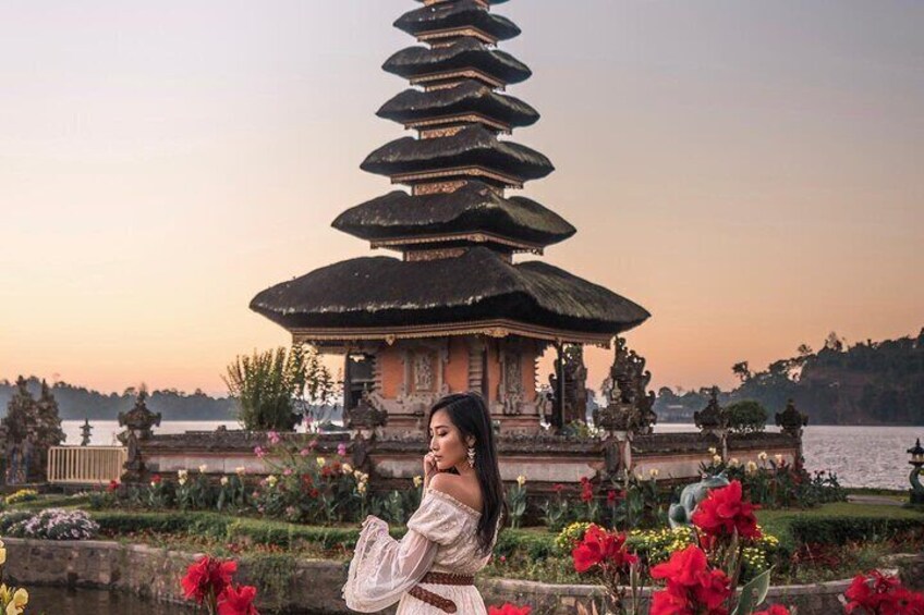 A pagoda-style structure with a tiered roof, surrounded by a garden with red flowers and a body of water in the background. 2