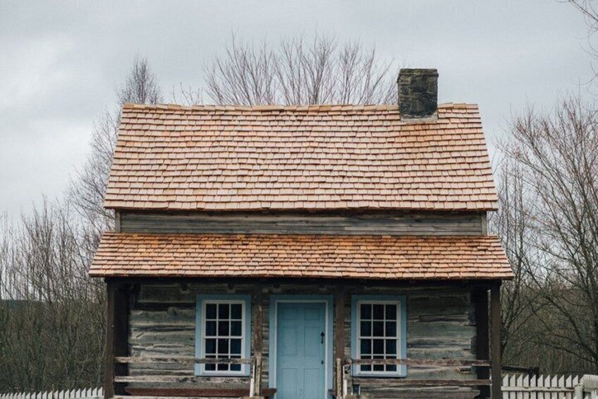 A rustic log cabin with a blue door and windows, surrounded by a white picket fence. 2