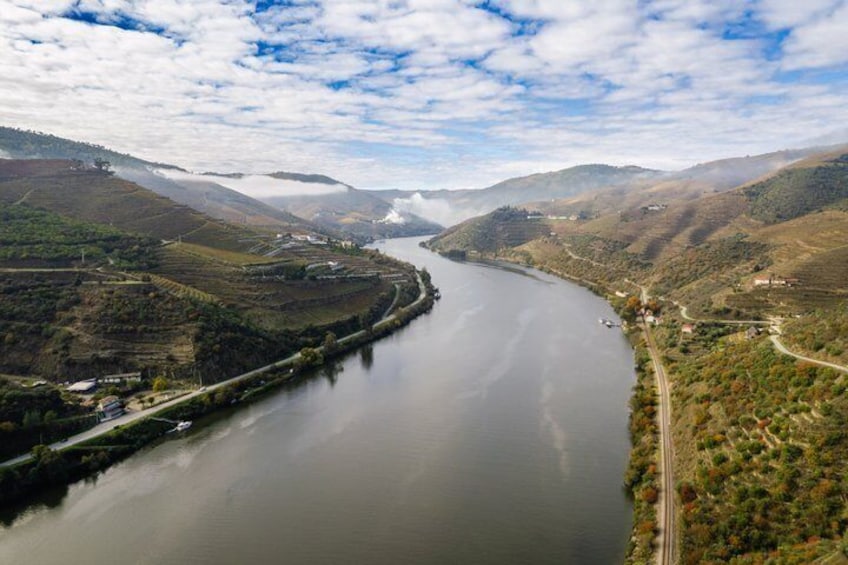 A river winding through a valley with hills on either side, a road along the river, and a small settlement near the water's edge. 3
