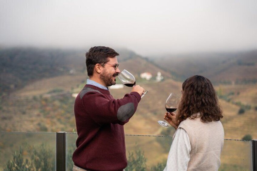 Two people tasting wine with a mountainous landscape in the background. 1