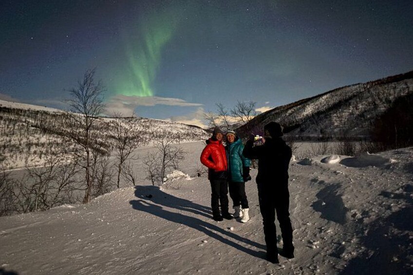 A snowy landscape with three people observing the night sky. 3