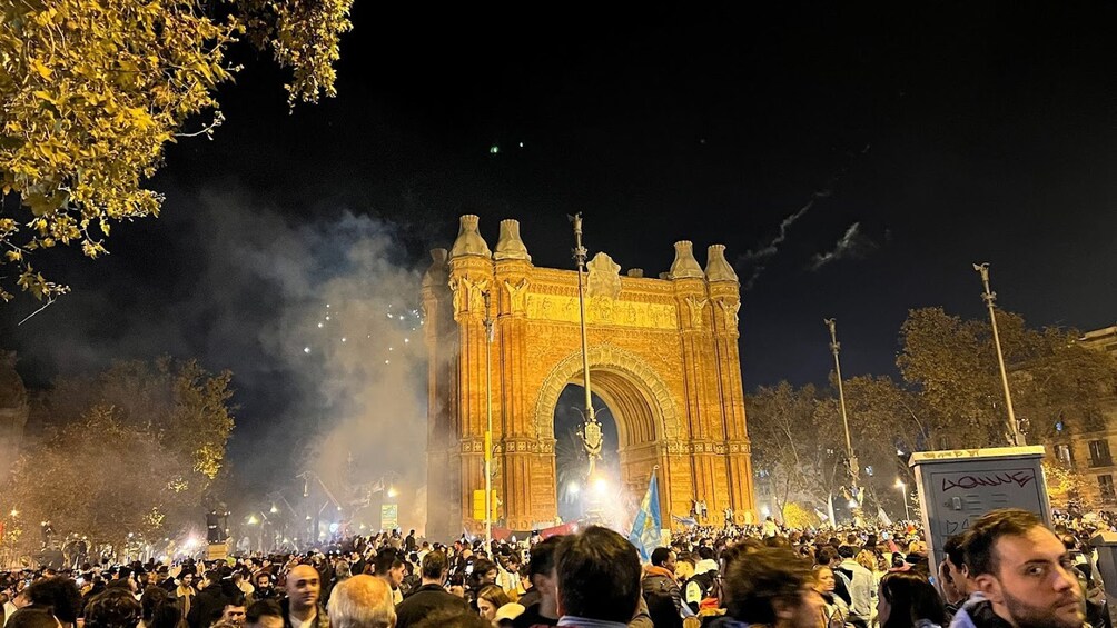 A large crowd gathered in front of a historic archway at night. 2