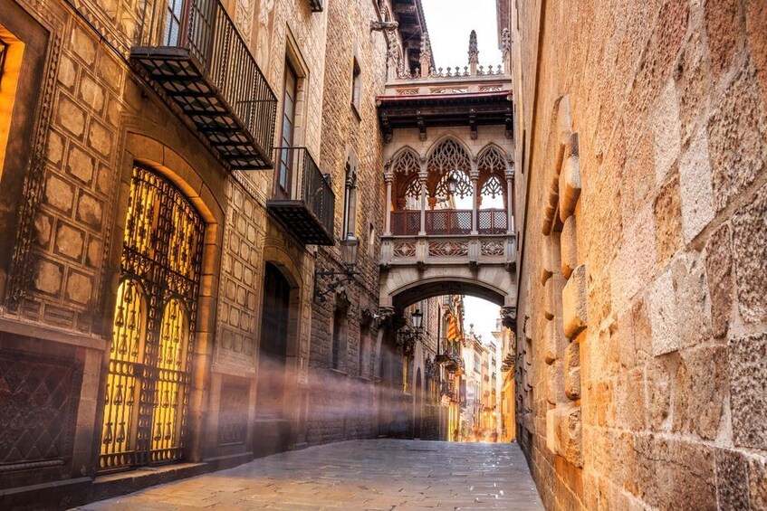 A narrow medieval street with stone buildings, ornate windows, and a wooden bridge. 1
