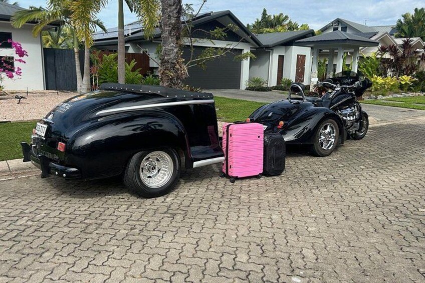 A black car with a trailer and a pink suitcase parked on a driveway. 2