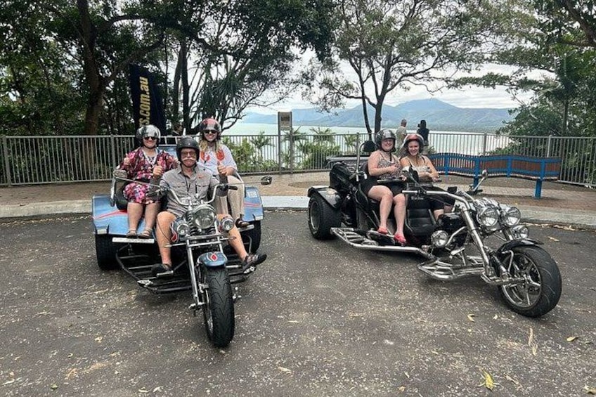 A group of people on a motorcycle and a tricycle, with a scenic view in the background. 3