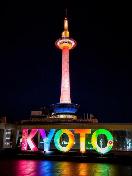 A tower with a lit top and a colorful sign with the letters 'KYOTO' below it. 1