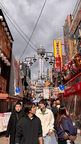 A busy street with people walking, a tower, and various signs and advertisements. 4