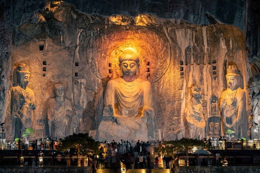 A large Buddha statue carved into a cliff face, surrounded by smaller statues and a crowd of visitors. 1