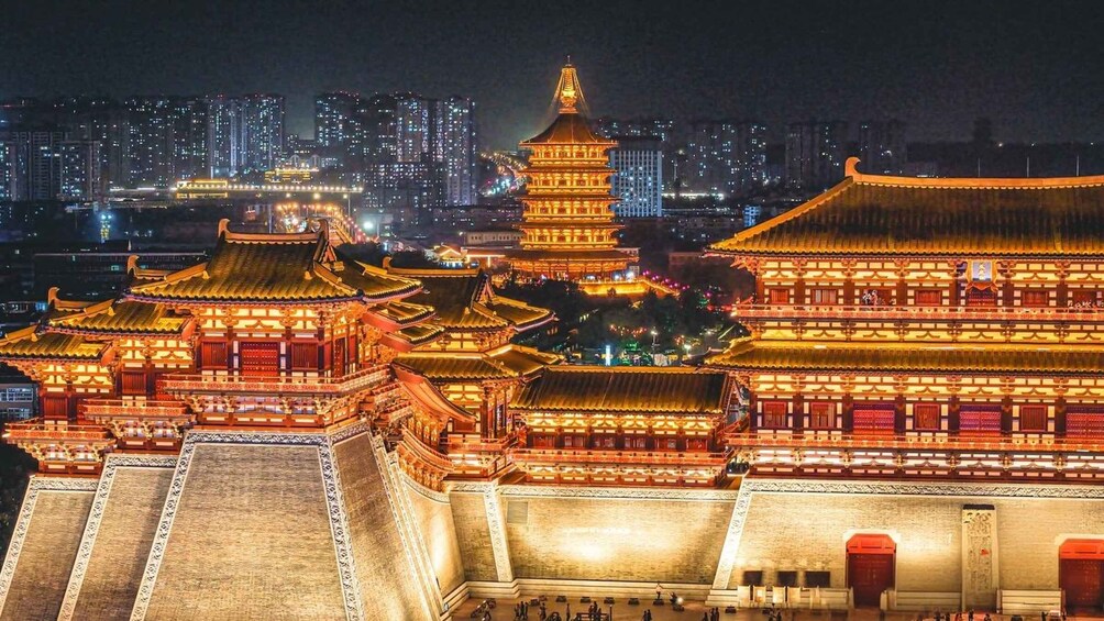 A traditional Chinese architectural complex with illuminated pagodas and a large building, set against a city skyline at night. 5