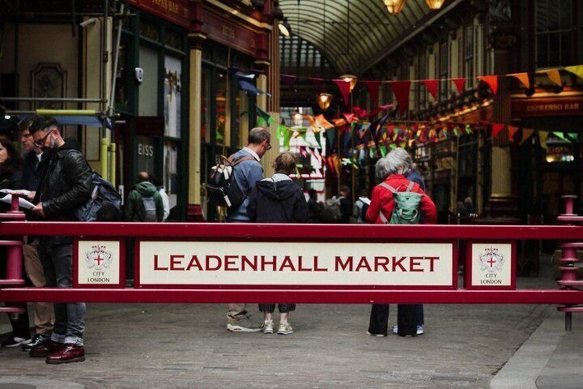 The Leadenhall Market with people standing in line, a red barrier, and the market's signage. 5