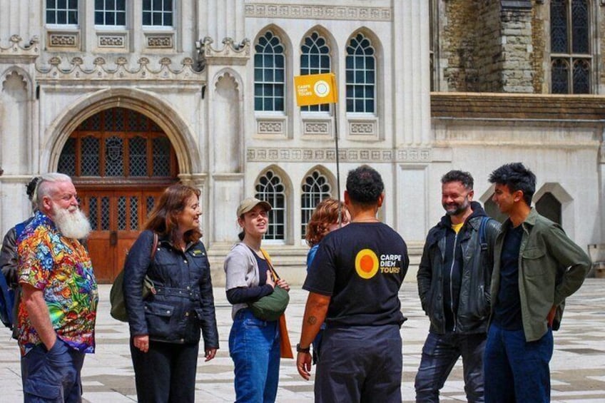 A group of people standing in front of a historic building with arched windows and a large wooden door. 1