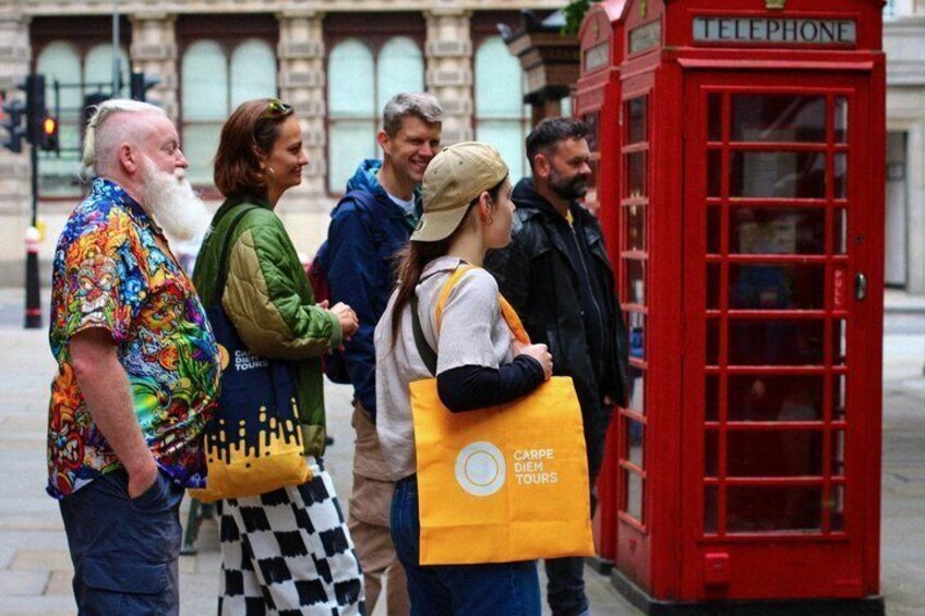 A group of people standing near a red telephone booth. 4