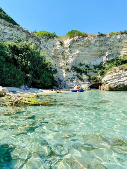 A clear coastal area with rocky cliffs, a sandy beach, and a calm sea. 4
