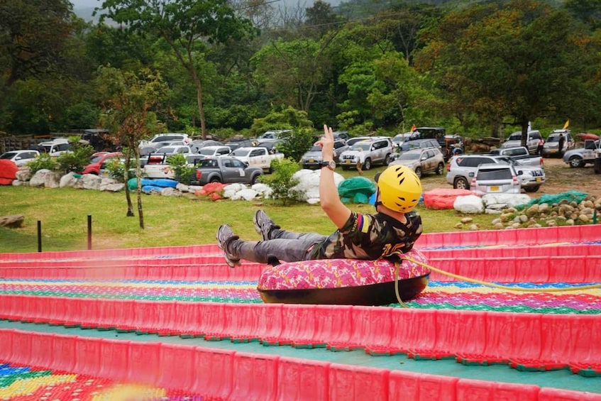 A person sliding down a colorful water slide in a park with cars parked in the background. 2