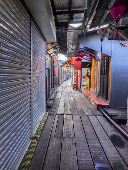 A narrow alley with closed shop shutters, wooden flooring, and hanging decorations. 4