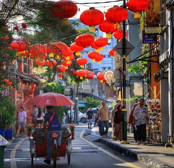 A street decorated with red lanterns, a bicycle rickshaw, and people walking. 2
