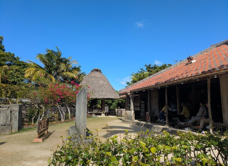 A traditional thatched-roof hut, a stone monument, and a building with a tiled roof, surrounded by tropical vegetation and palm trees. 3