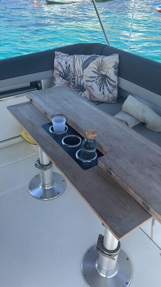 A boat's deck with a wooden table, cushions, and a bottle of water. 4