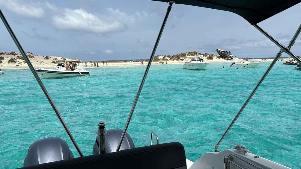 A boat on turquoise water with a sandy beach and other boats in the background. 5