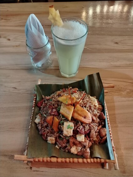 A meal with rice, vegetables, and meat on a banana leaf, accompanied by a glass of a light-colored beverage and a small bowl of soup. 5