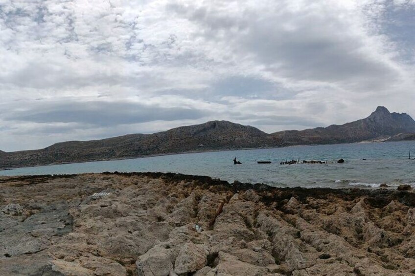 A rocky shoreline with calm water, distant mountains, and a cloudy sky. 2