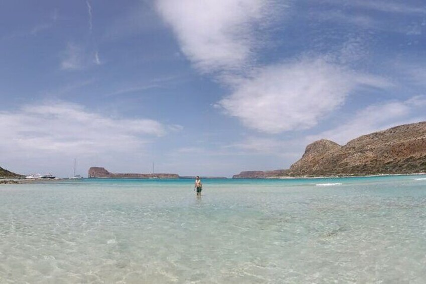 A person standing in shallow water with clear skies and distant rocky hills. 3