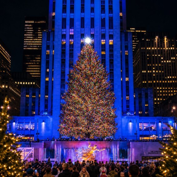 A large illuminated Christmas tree in front of a building with a stage and audience. 3