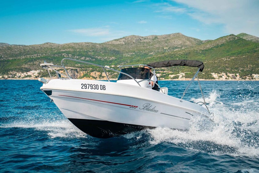 A white speedboat with the number 297930 DB on the bow, moving through the water with a mountainous landscape in the background. 4