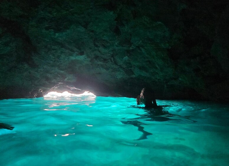 A cave with clear turquoise water and a person swimming. 2