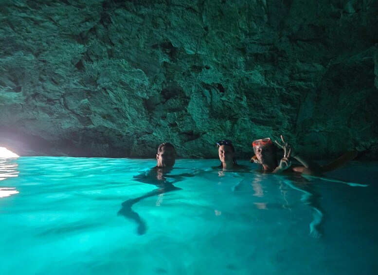 A group of people swimming in a clear blue pool with a rocky cave wall in the background. 3