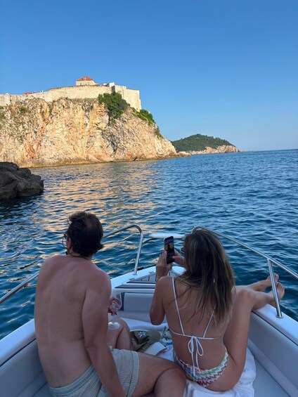 A boat with two people, one holding a camera, and a castle on a cliff in the background. 3