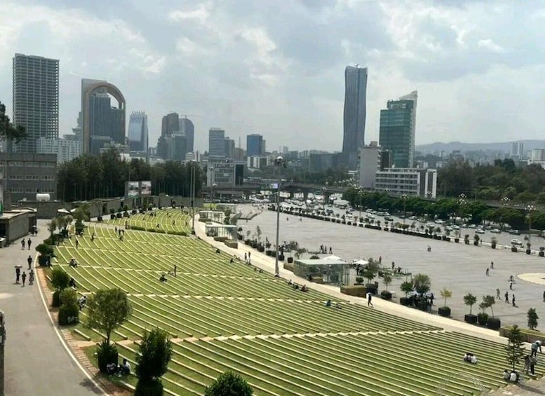 A cityscape with modern buildings, a large open square, and rows of graves. 1