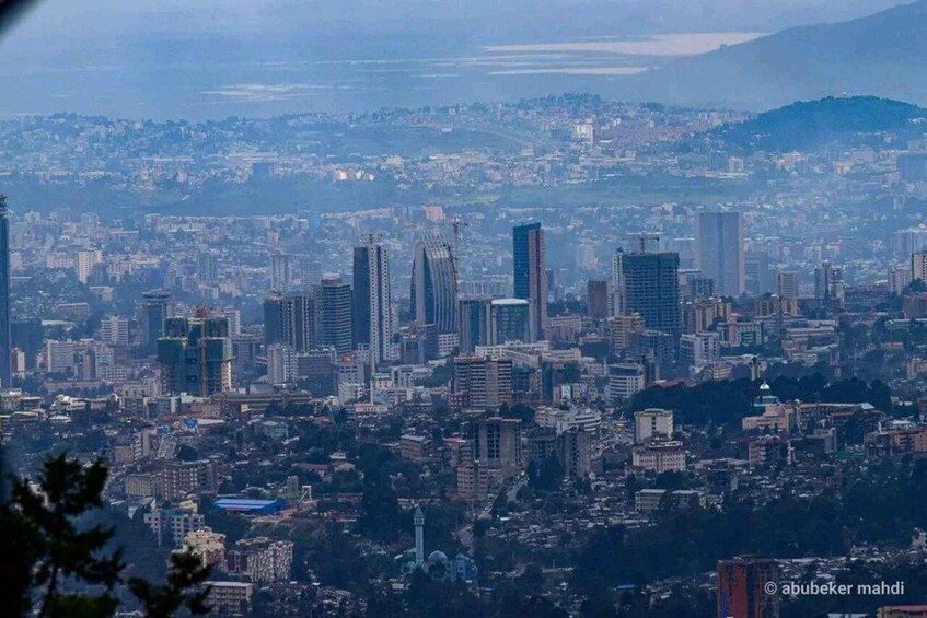 A cityscape with numerous high-rise buildings, a prominent mosque, and a hilly backdrop. 2