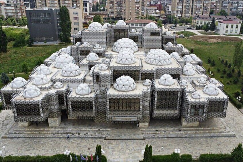 A large, geometric structure with multiple domed roofs, surrounded by a landscaped area and residential buildings in the background. 3