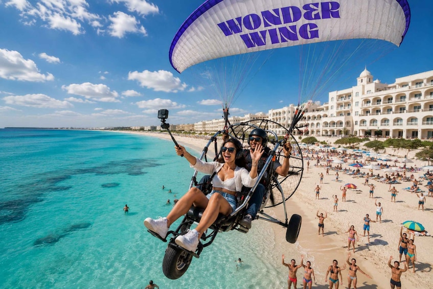 A person on a tandem paragliding adventure over a beach with clear turquoise waters and a resort in the background. 2