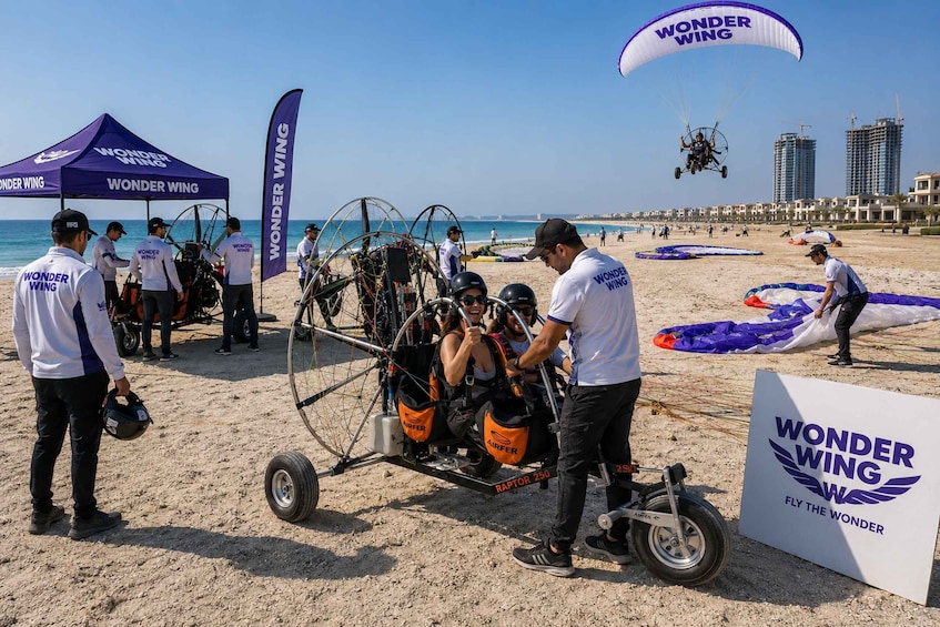 A beach with a parachute activity setup, including a cart with passengers and a parachute labeled 'WONDER WING.' 5