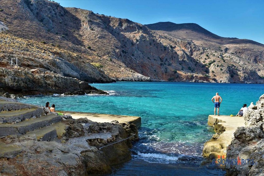A rocky coastline with clear turquoise waters, steps leading down to the sea, and a person standing on a platform. 4